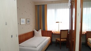 A hotel room with a bed, desk, chair, and curtains.