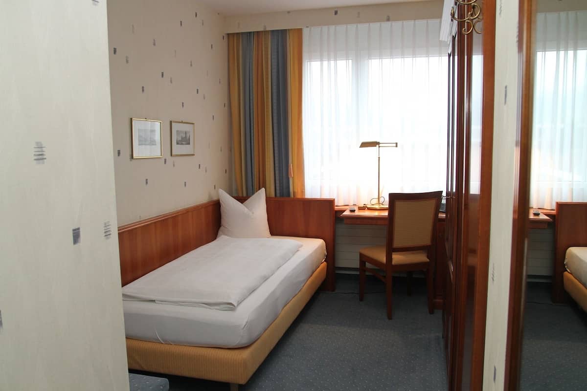 Ein Hotelzimmer mit Bett, Schreibtisch, Stuhl und Vorhängen.