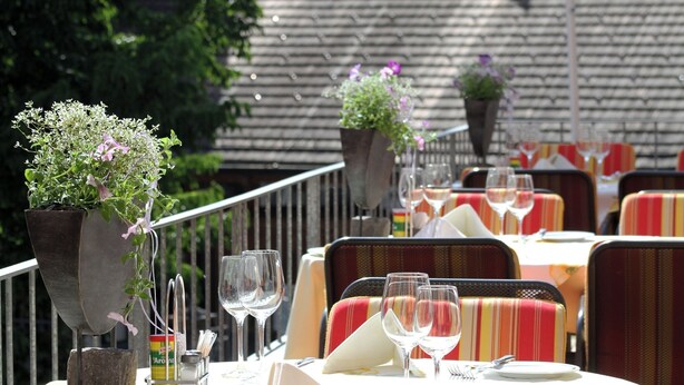 A restaurant with outdoor seating, tables set with wine glasses, plates, and cutlery.