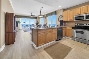A spacious kitchen with wooden cabinets, stainless steel appliances, and a view to a balcony. - 🌞Gulf FRONT | Stunning Views | Pool | Grandview East 1505🌞 (Panama City Beach)