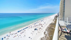 Blick auf einen Strand vom Balkon aus, mit blauem Himmel, Sandstrand und einem Pier in der Ferne.