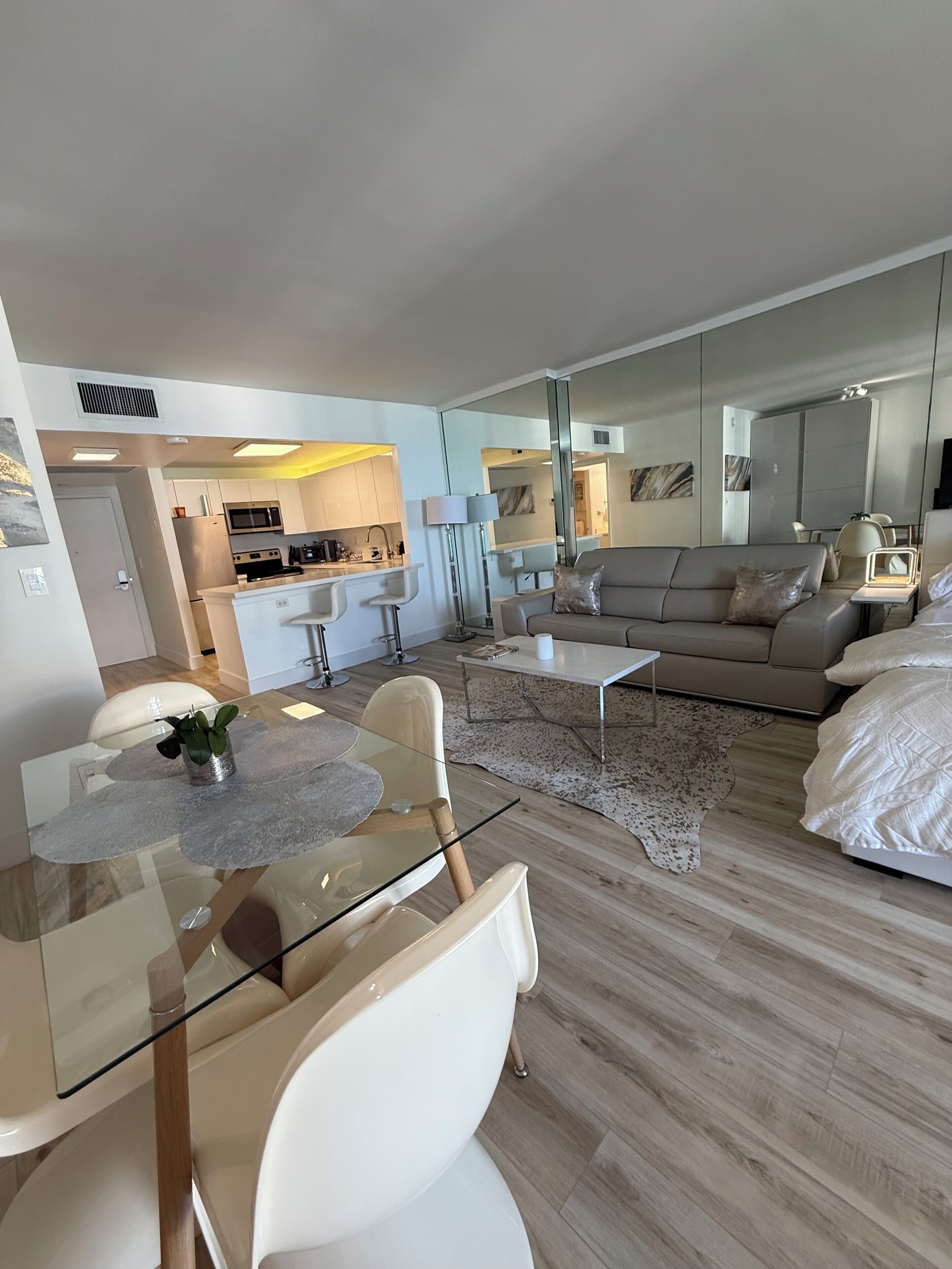 Een moderne woonkamer met een glazen eettafel, een bank en een keuken op de achtergrond.
