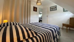 Un dormitorio con cama, una silla, una lámpara colgante y una puerta que da al baño.