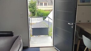 Una habitación con puerta corredera que da a un balcón, un sofá gris, una mesita y una silla.