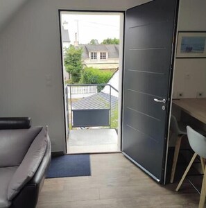 Ein Zimmer mit einer Schiebetür, die auf einen Balkon führt, einem grauen Sofa, einem kleinen Tisch und einem Stuhl.
