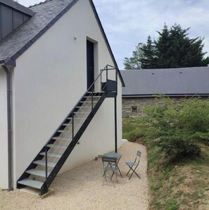Ein Gebäude mit einer Treppe, die zu einer Tür führt, einer kleinen Außen-Sitzgelegenheit mit Tisch und Stühlen sowie einem Kiesweg.