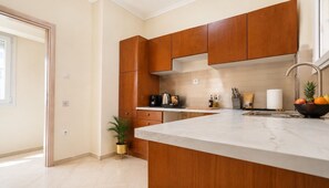 A modern kitchen with wooden cabinets, a marble countertop, and a small island. - D-Suites – Executive Sea View City Centre Apartment (Thessaloniki)