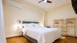 Ein Schlafzimmer mit einem Bett, einer Klimaanlage, einem Deckenventilator, einem Kleiderständer aus Holz und einem Lichtschalter.