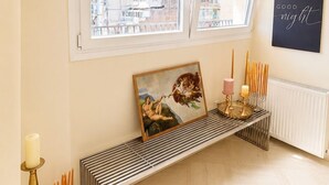 Ein Zimmer mit einer Bank, einem Heizkörper, einem Wandbild und einem Fenster mit Blick auf Gebäude.