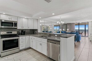 A modern kitchen with stainless steel appliances, a central island, and a view to a balcony with a pool. - Sand Castle III 204 - GULF FRONT SPIRAL STAIRCASE (Indian Shores)