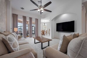 A modern living room with a ceiling fan, a flat-screen TV, and a dining area in the background. - CP948 - 6BR house with pool near Disney area (Davenport)