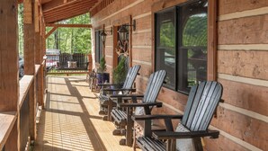 A wooden deck with Adirondack chairs, a wooden railing, and a view of the forest.