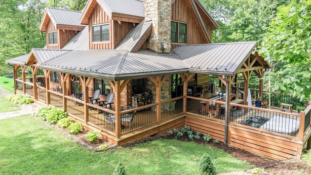 A cabin with a covered deck, a stone chimney, and a large window.