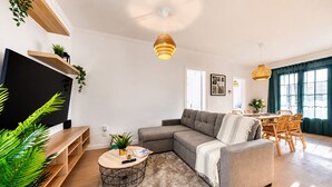 Ein modernes Wohnzimmer mit einer Eckcouch, einem runden Couchtisch, einem Fernseher und einem Essbereich mit Tisch und Stühlen.
