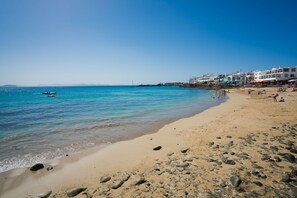 A beach with clear water, a boat, and buildings in the background. - Casa Lanzarote Luxury Stay • Beach 2 min • LVH (Playa Blanca)
