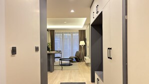 Moderni hotellihuone, jossa on työpöytä, tuoli, lamppu ja vaatekaappi.