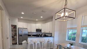Una cocina moderna con armarios blancos, un refrigerador de acero inoxidable, un microondas y una mesa de comedor de madera con sillas.