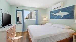 Un dormitorio con cama, televisión, cómoda, lámpara y aire acondicionado.