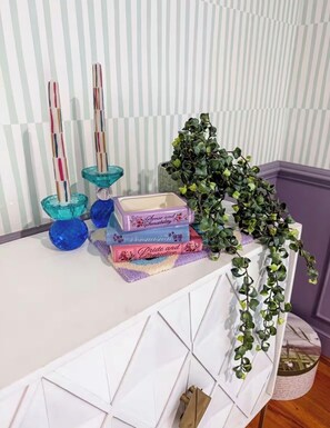 A white table with a geometric pattern, a stack of books, two blue glass candle holders, and a green plant. - The Joyful Escape | Playful 70s-Modern Retreat (Crewe)