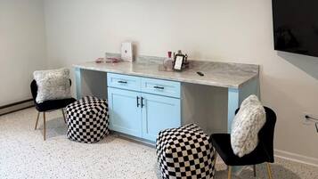 A modern kitchen with a marble countertop, two black chairs with checkered ottomans, a white cabinet, and a mounted flat-screen TV.