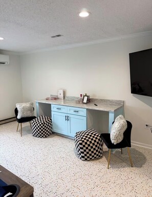 A modern kitchen with a marble countertop, two black chairs with checkered ottomans, a white cabinet, and a mounted flat-screen TV. - The Joyful Escape | Playful 70s-Modern Retreat (Crewe)