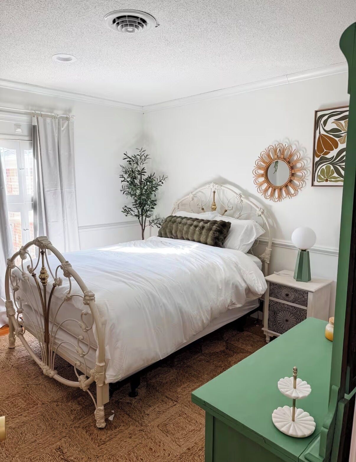 A bedroom with a white bed, a green nightstand, a decorative mirror, and a plant.