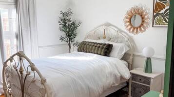 A bedroom with a white bed, a green nightstand, a decorative mirror, and a plant.
