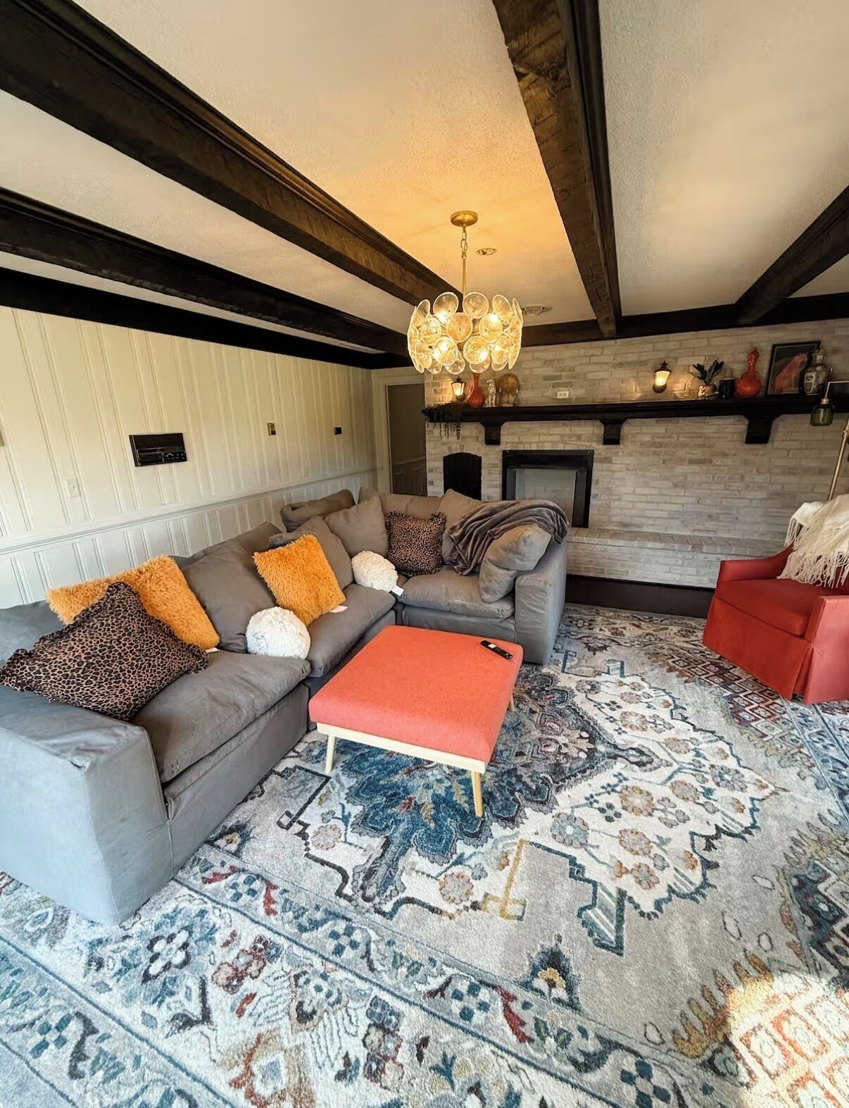 A modern living room with a sectional sofa, a red ottoman, patterned rugs, a fireplace, and a decorative ceiling light.