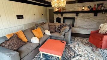 A modern living room with a sectional sofa, a red ottoman, patterned rugs, a fireplace, and a decorative ceiling light.