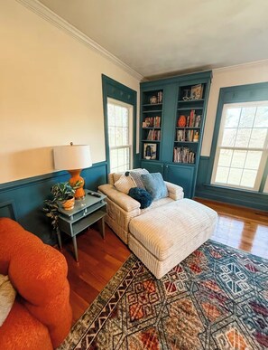A cozy living room with a sofa, a patterned rug, and a bookshelf. - The Joyful Escape | Playful 70s-Modern Retreat (Crewe)