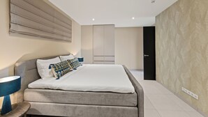Ein modernes Schlafzimmer mit einem großen Bett, Nachttischlampen, einem Kleiderschrank und einer Tür.