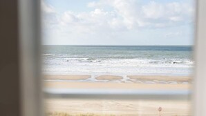 Vista de una playa a través de una ventana, con arena y cielo despejado.