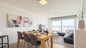 Una sala de estar moderna con comedor, ventanas grandes y vista al mar.