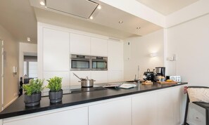 A modern kitchen with white cabinets, stainless steel appliances, and a black countertop. - Lavistamare - wake up with a sea view (Westende)