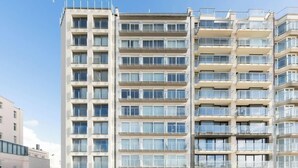Un edificio residencial de varios pisos con balcones, ventanas amplias y cielo despejado.