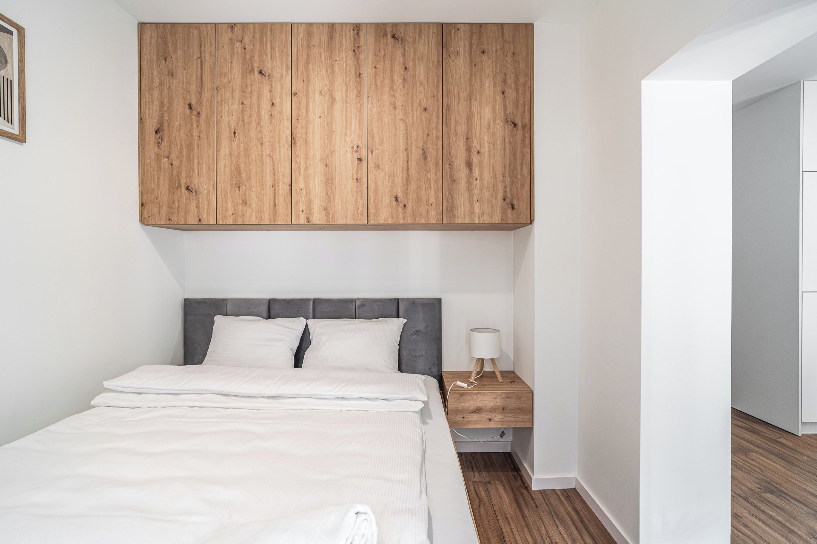 A bedroom with a bed, a nightstand, a wooden wardrobe, and a white wall.