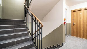 Una escalera con barandillas negras y pasamanos de madera, una puerta de madera y un detector de incendios en la pared.
