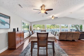 A dining area with a table, chairs, a ceiling fan, a sofa, and large windows. - Mimosa House - 5 bdrm house with large dock! (Rocky Mount)