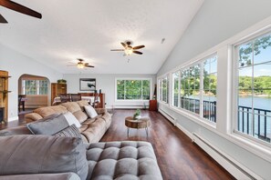 A spacious living room with a large sofa, a dining area, and a view of a lake. - Mimosa House - 5 bdrm house with large dock! (Rocky Mount)