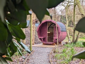 Eine zylindrische Holzhütte mit Tür, umgeben von Bäumen und Kies.