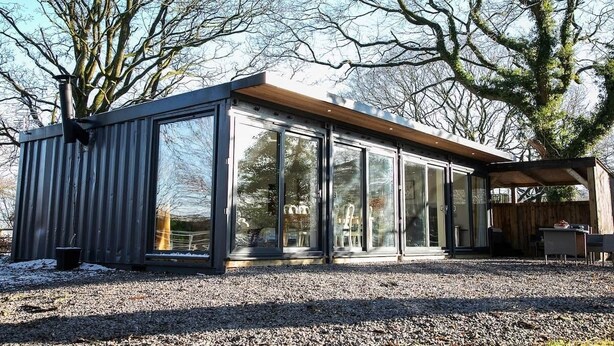 Un bâtiment moderne, de plain-pied, doté de grandes fenêtres en verre, d’une terrasse en bois et d’un sol en gravier.