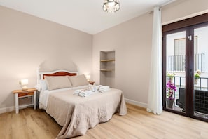 Un dormitorio con cama, mesitas de noche, armario y balcón con barandilla, además de una planta en maceta.