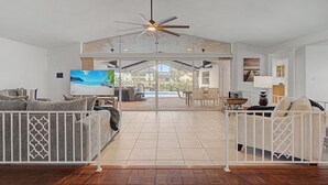 A spacious living area with a ceiling fan, a television, and a view of the outdoor patio. - Canal Front Retreat | Pool, Hot Tub, Dock + Game Room (Apollo Beach)