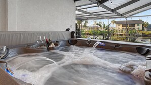 A hot tub with multiple jets, a glass, and bottles, set in a covered area with a view of a building and palm trees. - Canal Front Retreat | Pool, Hot Tub, Dock + Game Room (Apollo Beach)