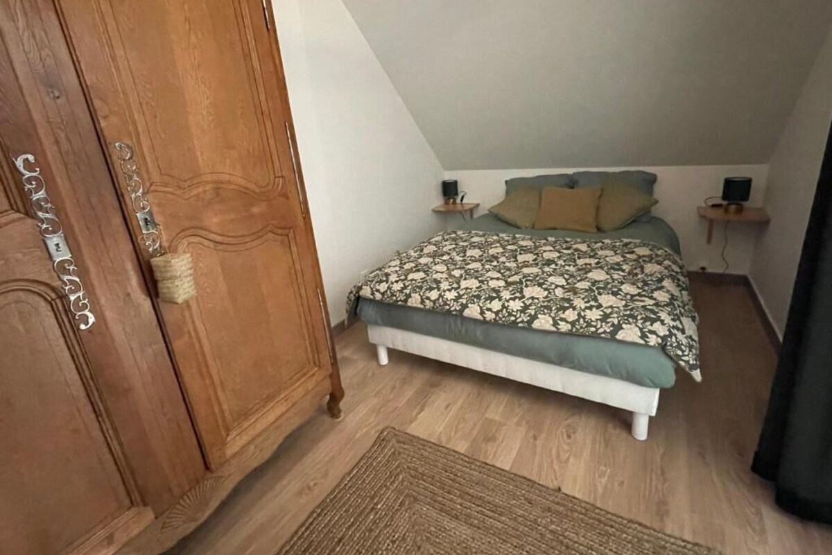 Un dormitorio con cama, armario de madera, mesita de noche con lámpara y una pequeña estantería con altavoz.