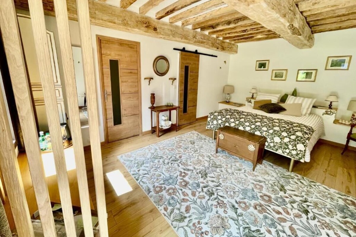 Un dormitorio con techo de madera, una cama con ropa de cama floral, una mesita de noche, un espejo y una puerta.