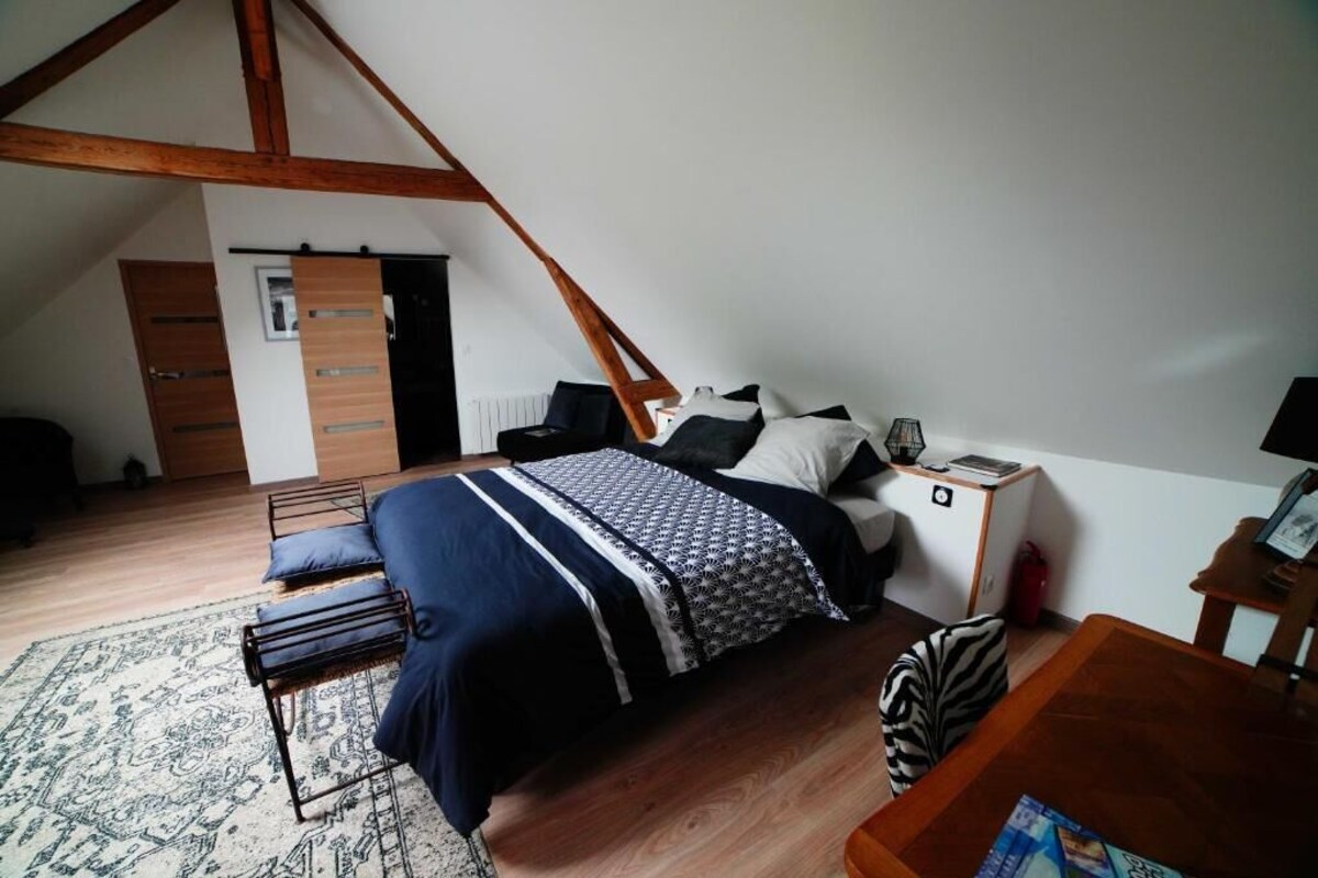 Un dormitorio con techo inclinado, una cama con ropa de cama estampada, una mesita de noche, una lámpara y una alfombra.