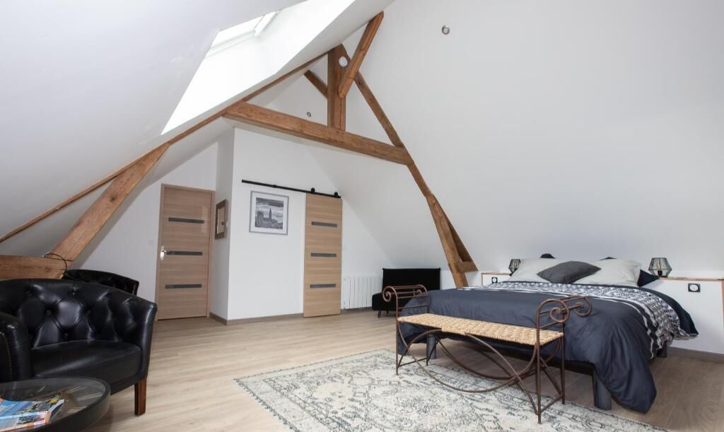 A loft bedroom with a sloped ceiling, a bed, a chair, a bench, and a wardrobe.