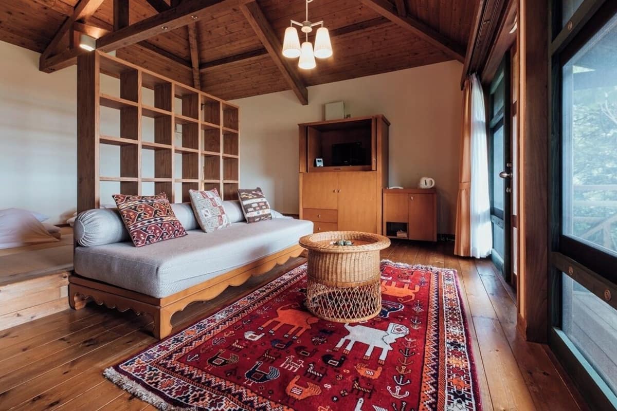 Ein gemütliches Zimmer mit Holzboden, einem Sofa mit gemusterten Kissen, einem gewebten Couchtisch und einem großen Fenster mit Blick.