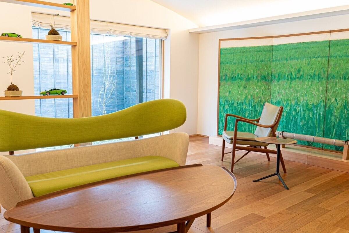 Une pièce avec un plancher en bois, un canapé vert, une table en bois, une chaise et une grande fenêtre donnant sur un paysage verdoyant.